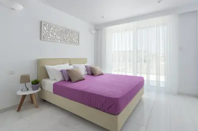 a white bedroom with a large bed with purple sheets at Maria & Nada Beachfront Villas in Kolimbia