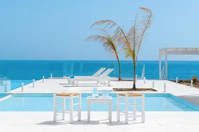 a pool with two white stools and a table and chairs at Maria & Nada Beachfront Villas in Kolimbia