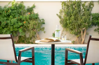 a table with a book and a bottle and two chairs at Mitsis Rodos Village in Kiotari