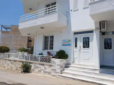 a white house with a porch and a door at Haraki Sunrise Apartments in Haraki