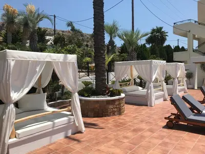a row of white beds on a patio with palm trees at Pefkos Blue in Pefki Rhodes