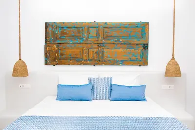 a bed with two blue pillows and a painting on the wall at Lindos Portes Suites - Adults Only in Líndos