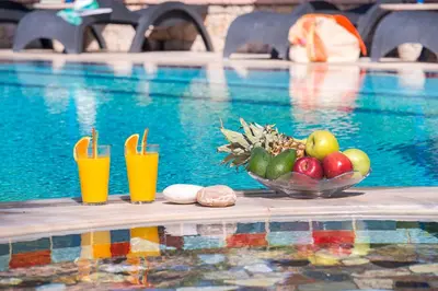 a bowl of fruit and drinks on a table near a swimming pool at Elefteria Apts & Suites in Kolimbia