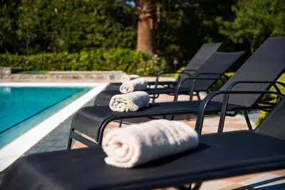 a row of black chairs with towels on them next to a swimming pool at Royal Classico Villa in Kolimbia