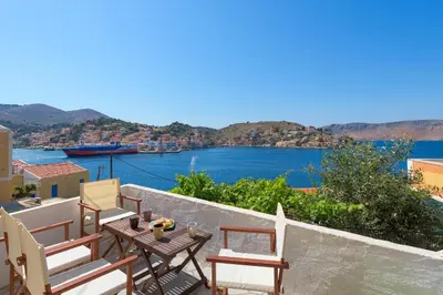 a balcony with chairs and a table with a view of the water at Aegli Villa by Blue Wave in Symi