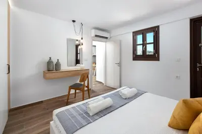 a white bedroom with a bed and a chair at Lindos Heart Apartments in Líndos