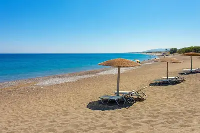 three beach chairs and umbrellas on a beach at Horizon Line Villas in Kiotari