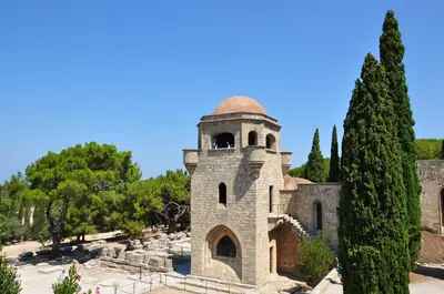 a building with a tower in a park with trees at Vivian Studios in Ialyssos