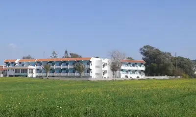 a large white building with a field in front of it at Nirvana Beach Hotel in Theologos