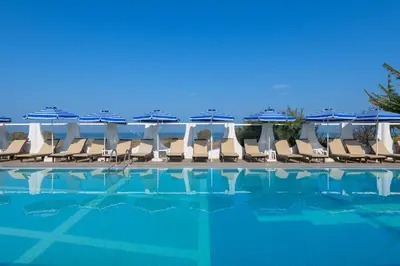a group of chairs and umbrellas next to a swimming pool at Nirvana Beach Hotel in Theologos