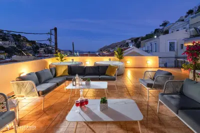 a patio with couches and tables on a roof at Maravelia's Rooms in Symi