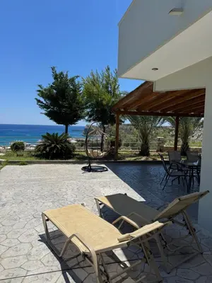 a couple of chairs sitting on a patio with the ocean at Villa Rose in Archangelos