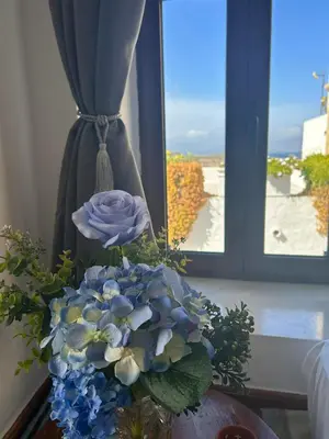 a vase of blue flowers on a table in front of a window at New Lindos Studio 45 renovated in Líndos