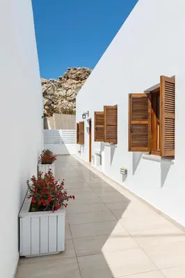a white building with wooden shutters and flowers on it at Traditional Lindian Suites in Líndos