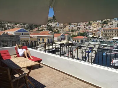 a woman sitting on a balcony looking out at the harbor at Captain's Suites in Symi