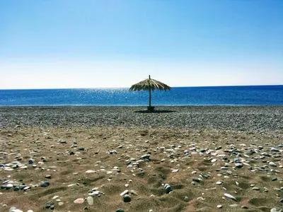 a straw umbrella on a rocky beach near the ocean at Ktima Tzaneti in Lachania