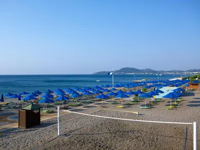 a beach with blue umbrellas and chairs and the ocean at Esperides Beach Resort in Faliraki