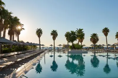 a swimming pool with chaise lounges and palm trees at Esperides Beach Resort in Faliraki