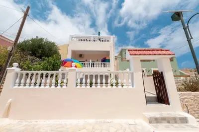 a white house with a balcony with a colorful umbrella at Filoxenia Apartments in Halki