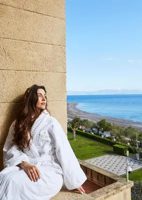 a woman in a white robe sitting on a wall next to the ocean at Grande Albergo Delle Rose in Rhodes Town