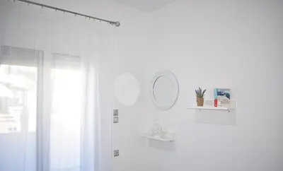 a white bathroom with a mirror and a window at Levande Studio with private parking in Afantou