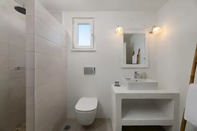 a white bathroom with a toilet and a sink at Stegna Akti Luxury Suites in Archangelos