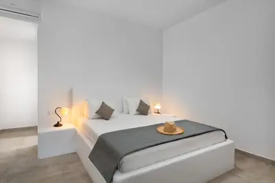 a white bedroom with a white bed and two lamps at Stegna Akti Luxury Suites in Archangelos
