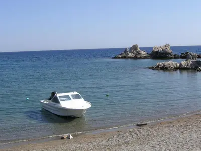a white boat sitting on the shore of a beach at Maria Studios and Apartments in Haraki