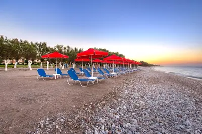 a row of chairs and red umbrellas on a beach at Bayside Hotel Katsaras in Kremasti