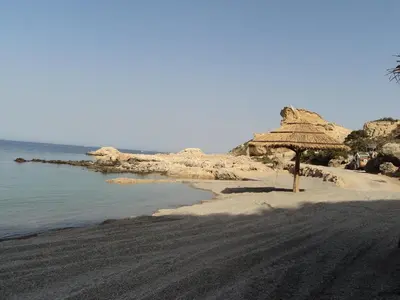 a beach with a straw umbrella and the ocean at Christos studios and family apartments in Rhodes Town