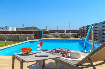 a table with a drink and a bowl of watermelon next to a pool at Lindos Topaz in Líndos