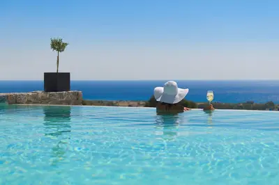 a woman in a hat in a swimming pool with a glass of wine at Alav Pool Villa in Afantou