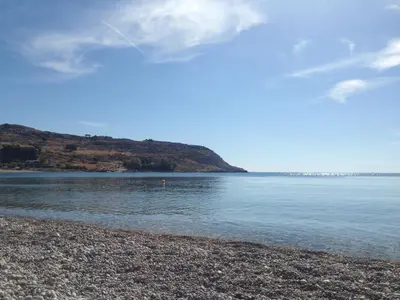 a body of water with a rocky beach and a hill at Haraki Blue Pearl in Haraki