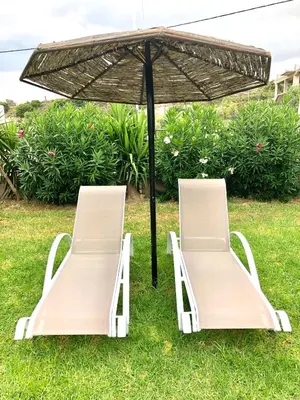 two chairs under an umbrella in the grass at Rose Hotel Faliraki in Faliraki