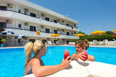 two women sitting next to a swimming pool with drinks at Butterfly Studios, Faliraki in Faliraki