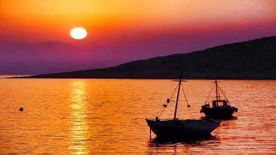 two boats sitting in the water at sunset at Amazing House in Halki in Halki