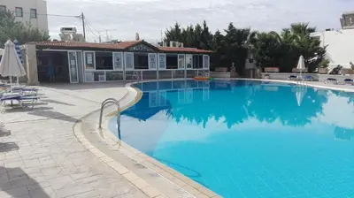 a large blue swimming pool with a house in the background at Coliseum Studios & Apartments in Pefki Rhodes