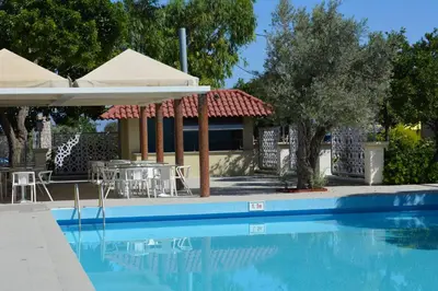 a swimming pool with a table and a building at Filerimos Village Hotel in Ialyssos