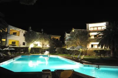 a large swimming pool with chairs and umbrellas at night at Niki Hotel Apartments in Ialyssos