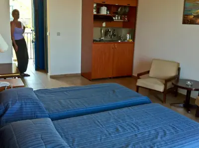 a bedroom with a blue bed and a woman in a kitchen at Castellania Hotel Apartments in Livadia