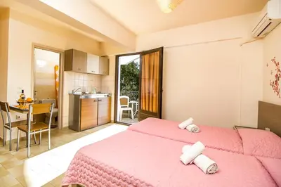 a bedroom with two pink beds and a kitchen at Takis Hotel Apartments in Ialyssos