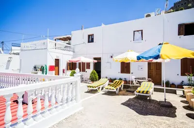 a white house with yellow and blue chairs and umbrellas at Villa Koki Studios in Líndos