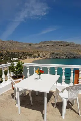 a white table and chairs on a balcony with water at Villa Koki Studios in Líndos