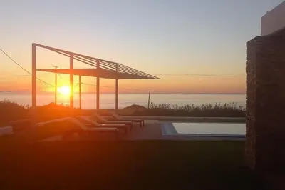 a sunset over a swimming pool with the sun setting at CRISTELIA SEAFRONT & POOL VILLA in Lachania