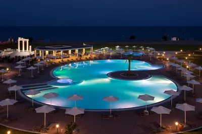 a large swimming pool with umbrellas at night at Apollo Blue in Faliraki