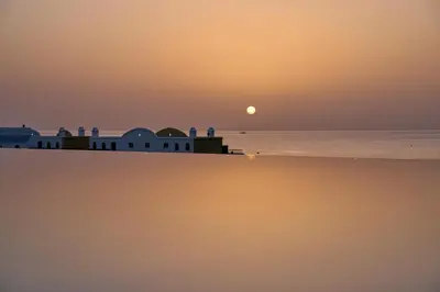 a sunset over the ocean with a building on the beach at Lindos Grand Resort & Spa - Adults Only in Líndos