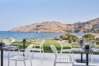 a patio with tables and chairs and a view of the water at Lindos Grand Resort & Spa - Adults Only in Líndos