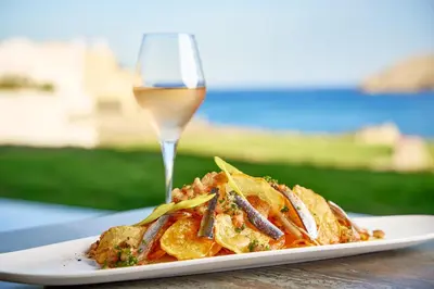 a plate of food and a glass of wine at Lindos Grand Resort & Spa - Adults Only in Líndos