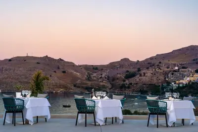 a restaurant with tables and chairs with a view of the water at Lindos Grand Resort & Spa - Adults Only in Líndos