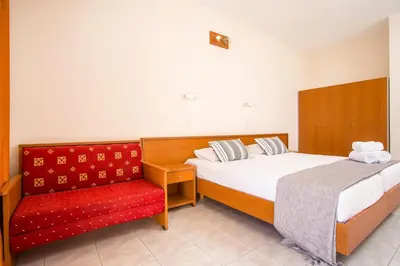 a bedroom with two beds and a red chair at Sam's Faliraki in Faliraki